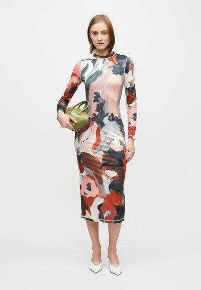 Langermet, kroppsnær kjole med abstrakte blomsterprint i rosa, rødt og grønt. Modellen holder en liten grønn veske og har på seg hvite høye hæler.