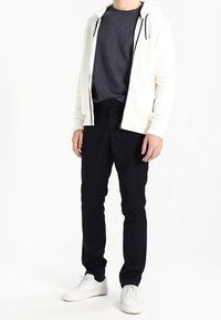 Biała bluza z kapturem z czarnym zamkiem i sznurkami, na ciemnoszarej koszulce, w połączeniu z granatowymi wąskimi spodniami i białymi trampkami.