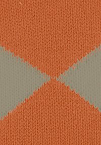 Tissu tricoté avec un motif en losanges orange et beige, présentant une texture visible et des fils entrelacés. Apparence textile douce et chaleureuse.