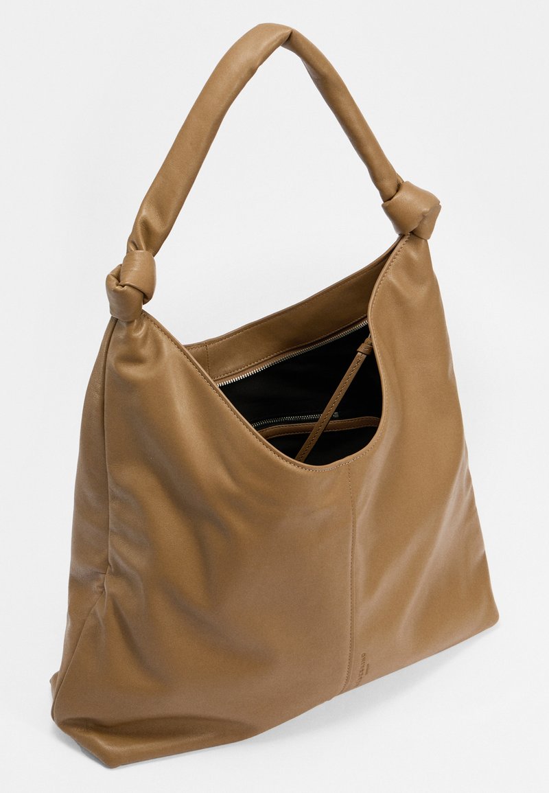 Braune Leder-Tote mit einem lässigen Design, geknotetem Griff und einem geräumigen Innenraum mit einem Reißverschlussfach. Glatte Textur.