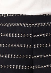 Μαύρο ύφασμα με λευκές ριγωτές σχέσεις, περιλαμβάνοντας αραιά γεωμετρικά σχήματα. Το ανώτερο μέρος είναι φτιαγμένο από κρεμώδες, ραβδωτό λευκό υλικό.