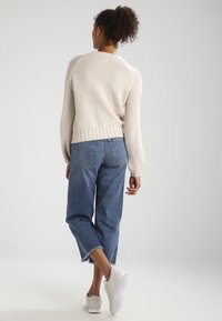 Lichtbeige gebreide trui met een gestructureerd patroon, gecombineerd met lichte, ruime spijkerbroeken en witte sneakers. Korte mouwen en geribbelde boorden.