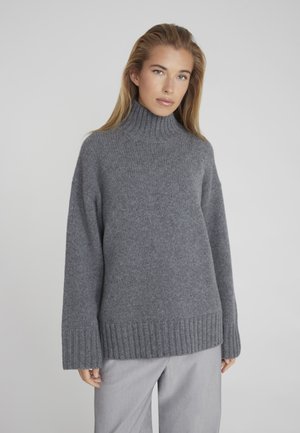 Grijze coltrui van zacht gebreid stof, met een relaxte pasvorm, ribgebreide boorden en onderrand. Gecombineerd met lichtgrijze broek.