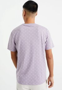 Lila bomulls t-shirt med ett upprepande vitt vågmönster, korta ärmar och en avslappnad passform med rundad nederkant.