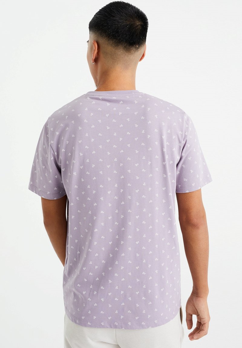 Lila bomulls t-shirt med ett upprepande vitt vågmönster, korta ärmar och en avslappnad passform med rundad nederkant.