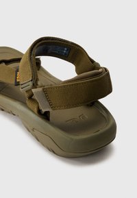 Olivengrønn sandal med teksturert gummisåle og justerbare stoffstropper. Har et logomerke og en løkke for sikker passform.