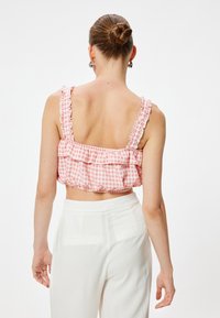 Top corto de cuadros rosa con tirantes de hombro con volantes. Presenta un diseño de cintura fruncida y espalda, combinado con pantalones blancos de cintura alta.
