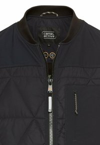 Marineblauer, gesteppten Bomberjacke mit geripptem Kragen. Sie verfügt über einen Reißverschluss vorne und eine Brusttasche mit Seilverzierung.