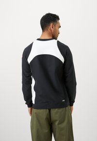 Sudadera negra con acentos texturales blancos y un diseño curvado en la parte trasera, con cuello redondo y puños acanalados.