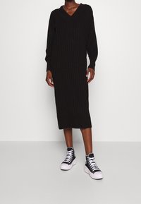 Abito midi nero a coste con scollatura a V e maniche lunghe, abbinato a sneakers alte nere con suole e lacci bianchi.