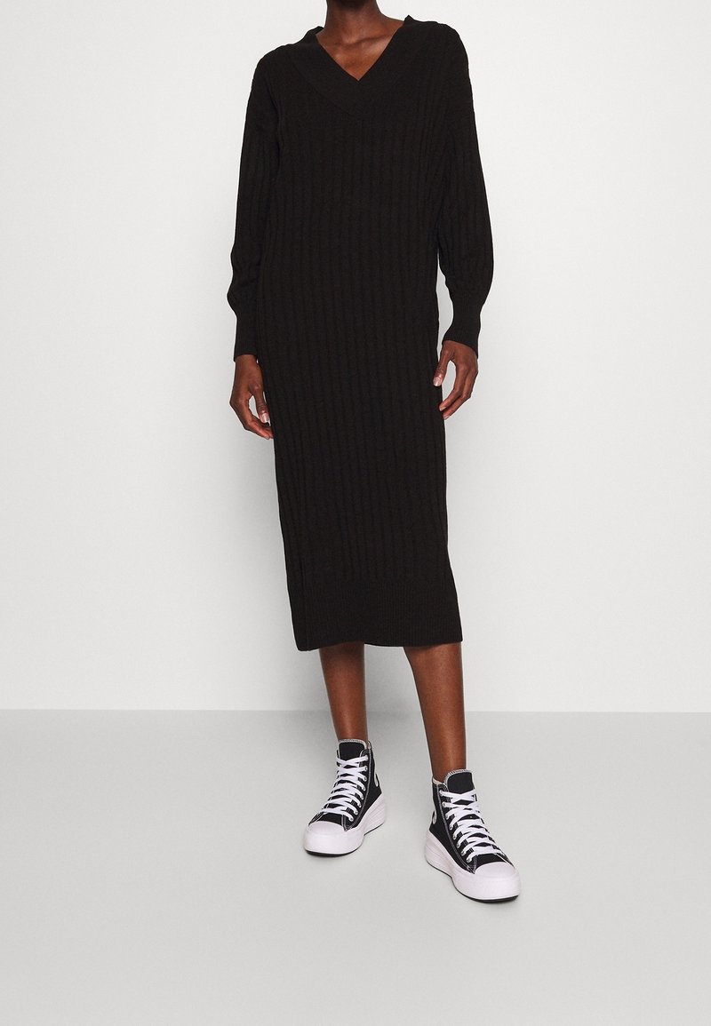 Abito midi nero a coste con scollatura a V e maniche lunghe, abbinato a sneakers alte nere con suole e lacci bianchi.