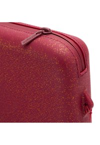 Custodia rossa texturizzata con un motivo di luccicante spruzzata dorata, dotata di una chiusura con zip liscia e di un piccolo manico laterale.