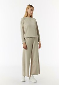 Beżowy zestaw odzieży domowej z długim rękawem i okrągłym dekoltem oraz spodniami o szerokich nogawkach. Wykonany z miękkiego, gładkiego materiału z delikatnym stretch.