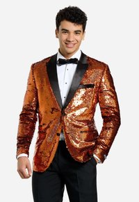 Blazer de lentejuelas con un patrón naranja y dorado, solapas de satén negro, cierre de un solo botón y pañuelo negro en el bolsillo. Lleva puesto sobre una camisa blanca y pajarita.