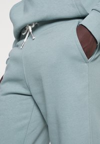 Lichtblauwe trainingsbroeken van een katoenmix met een zachte textuur. Voorzien van een trekkoord in de taille en contrasterende bruine zakaccenten.