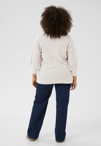 Sweter w kolorze kremowym z teksturowanym wzorem w zygzak, zestawiony z ciemnoniebieskimi szerokimi dżinsami. Sweter ma rękawy o długości trzy czwarte w stylu bufka.