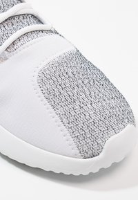 Grå och vit sportskor med en texturerad stickad överdel, släta vita detaljer och en rundad gummisula. Lättviktsdesign, minimalistisk stil.