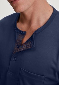 Marineblauwe korte mouwen shirt met een knoopsluiting in de hals, voorzien van een oranje geometrisch patroon op de knoopsluiting en een borstzak.