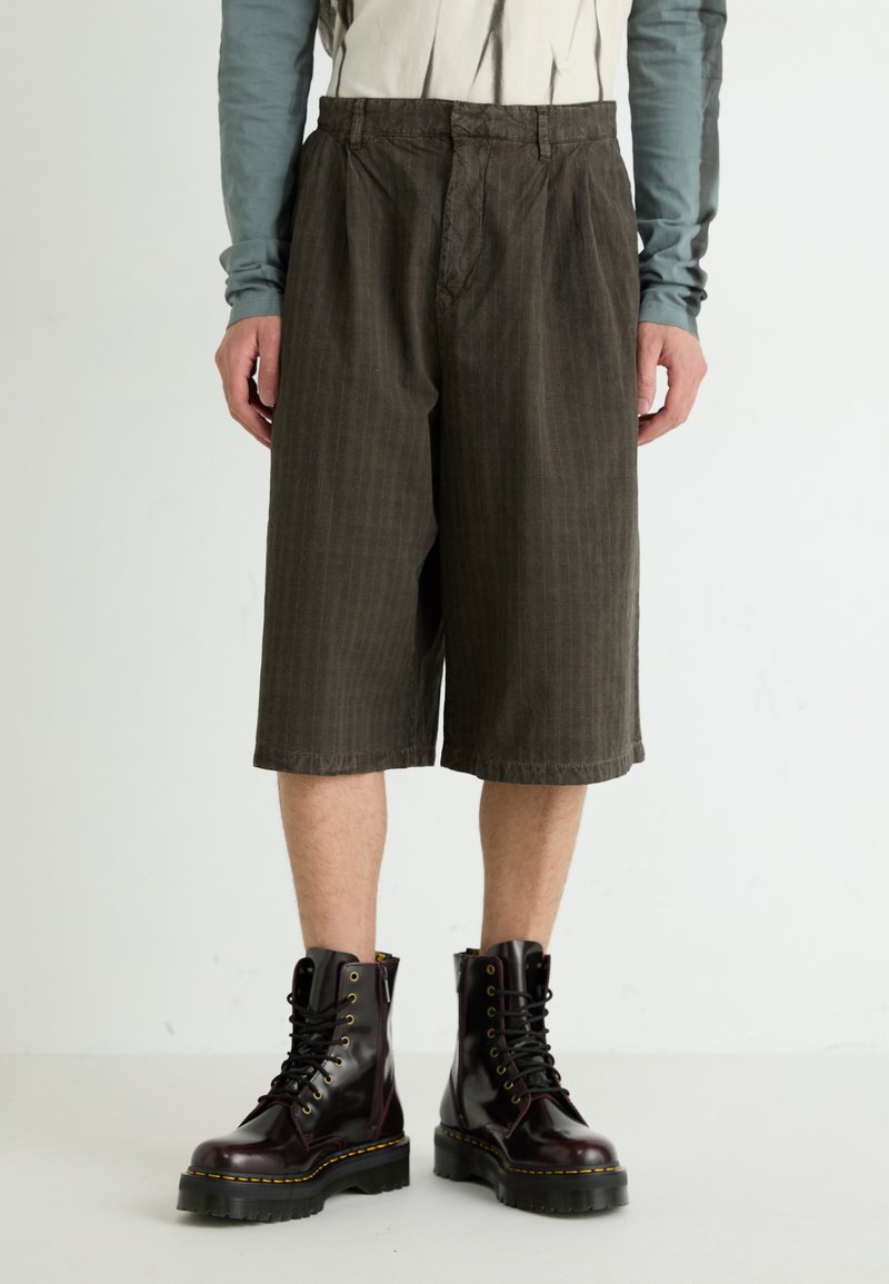 Shorts en velours côtelé marron avec des rayures verticales, présentant une coupe décontractée et un ourlet au genou, associés à des bottes en cuir bordeaux à lacets.