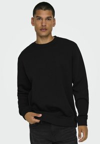 Zwarte crewneck sweatshirt gemaakt van een katoenmix, met ribgebreide cuffs en zoom, en een relaxte pasvorm. Draagt met donkere jeans, vastgehouden bij de zoom.