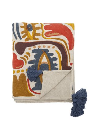 Tissu décoratif plié avec des motifs abstraits multicolores en rouge, moutarde, bleu et marron, avec des pompons bleus aux coins.