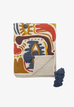 Tissu décoratif plié avec des motifs abstraits multicolores en rouge, moutarde, bleu et marron, avec des pompons bleus aux coins.