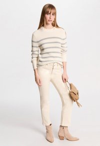 Pull en tricot rayé crème et gris, pantalon slim beige et bottes de cheville en daim tan. L'ensemble comprend un petit sac à main avec des franges.
