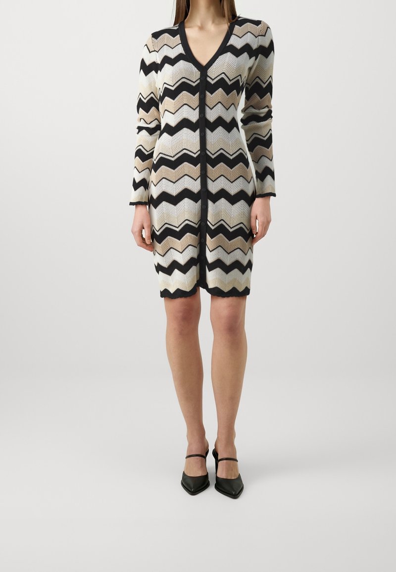 Robe en maille avec col en V, manches longues et motif en zigzag en marron, beige et noir. Fermeture boutonnée sur le devant.