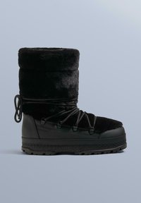 Sort pelsforet støvle med en glat læderbase, rundet tå og riflet sål. Har fleksible snørebånd og en blød, fyldig øvre skaft.