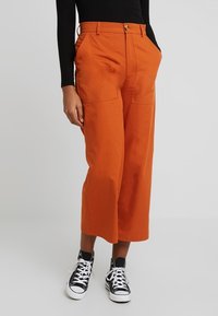 Oranje culottebroek van katoen, met twee voorzakken, een knoopsluiting en een wijd uitlopende broekstijl. Gecombineerd met zwarte sneakers.