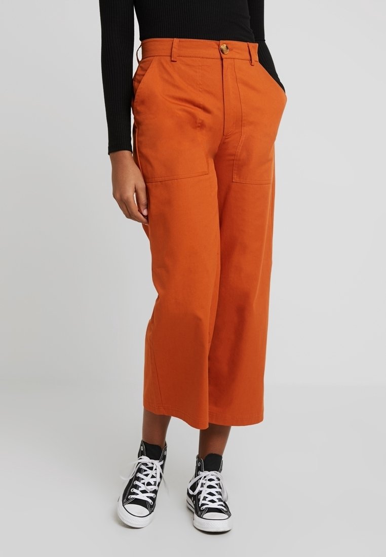 Oranje culottebroek van katoen, met twee voorzakken, een knoopsluiting en een wijd uitlopende broekstijl. Gecombineerd met zwarte sneakers.