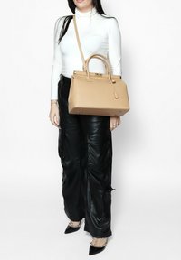 Borsa a mano in pelle beige con forma strutturata, manici superiori e tracolla removibile. Pantaloni cargo in ecopelle nera con tasche.