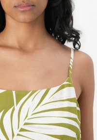 Haut sans manches vert et blanc à motif, avec un décolleté carré et des bretelles fines, présentant un tissu texturé avec un motif de feuilles.