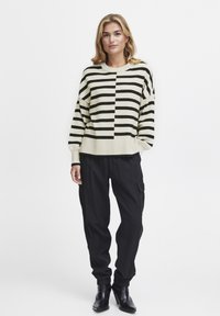 Gestreifter Pullover in Schwarz und Creme, mit boxy Fit und geripptem Saum, kombiniert mit schwarzen Cargo-Hosen und ankle boots.