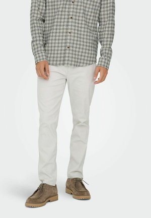 Camisa a cuadros en blanco y negro, combinada con pantalones gris claro y zapatos de ante marrón con suelas de goma y cordones.