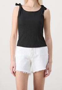 Débardeur noir côtelé à encolure carrée et bretelles nouées aux épaules, associé à un short en denim blanc effiloché.