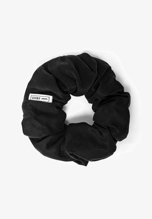 Czarna gumka do włosów z tkaniny o fakturowanym wykończeniu, z małą białą metką z napisem "SURF" i wzorem fali. Okrągły kształt, elastyczny materiał.
