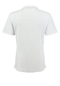 Camisa polo blanca de manga corta con un patrón texturizado, que presenta un cuello clásico y un dobladillo recto en la parte inferior.