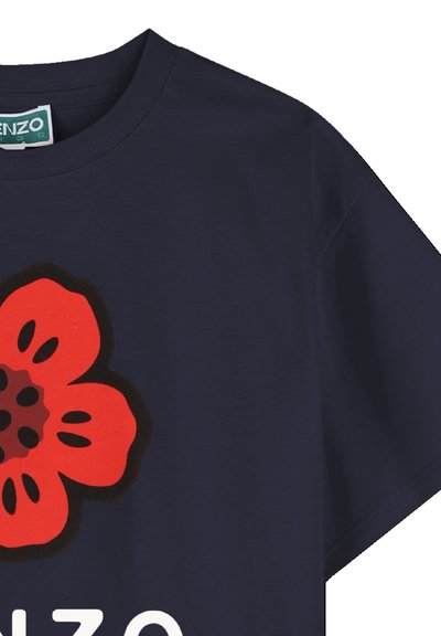 T-shirt bleu marine avec un grand motif de fleur rouge mettant en valeur des accents noirs. Manches courtes et col rond. Texte blanc sous le dessin.
