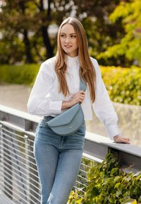 Světle modrá kožená kabelka s zaobleným tvarem a nastavitelným popruhem. Nositelná s bílou košilí na knoflíky a sladěná se světle modrými džínami.