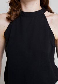 Haut noir sans manches avec un col montant et une coupe ajustée. Texture lisse et mate sans motifs visibles ni détails métalliques.