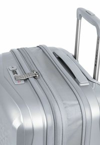 Valigia rigida argentata con superficie texturizzata, doppia cerniera, lucchetto combinato, manico estensibile e maniglia laterale per un trasporto facile.