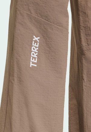 Bež hlače od tkanine s teksturom s bijelim uspravnim logotipom "TERREX" izvezenim na lijevom bedru.