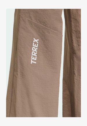 Pantaloni beige in tessuto strutturato con logo verticale bianco "TERREX" ricamato sulla coscia sinistra.