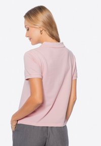 Krátký rukáv růžová polo tričko vyrobené z měkké tkaniny s plochým pleteným límcem a decentním přiléhavým střihem. Má ohrnuté rukávy a čistý konec.