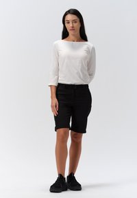 Zwarte shorts met een riem, gecombineerd met een witte top met driekwartmouwen. Model draagt zwarte sneakers en staat op een witte achtergrond.