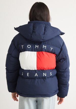 Navy blue puffer jacket with a large red and white panel design on the back, featuring the text "TOMMY JEANS" in white lettering.