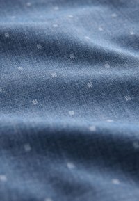 Niebieska tkanina o delikatnej fakturze, z małymi białymi kropkami na całej powierzchni, tworząca subtelny kontrast wizualny.