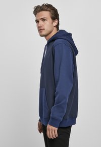 Felpa blu navy realizzata in tessuto morbido, dotata di una tasca frontale, cappuccio con cordino regolabile e polsini e orlo a coste.