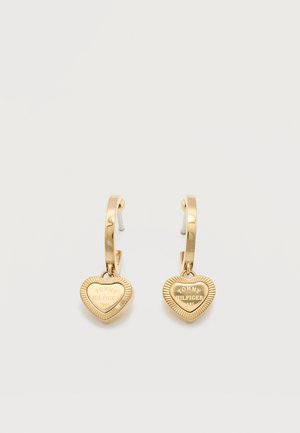Gold-tone hoop earrings with engraved heart-shaped pendants reading "Tommy Hilfiger 1985" on a plain white background.